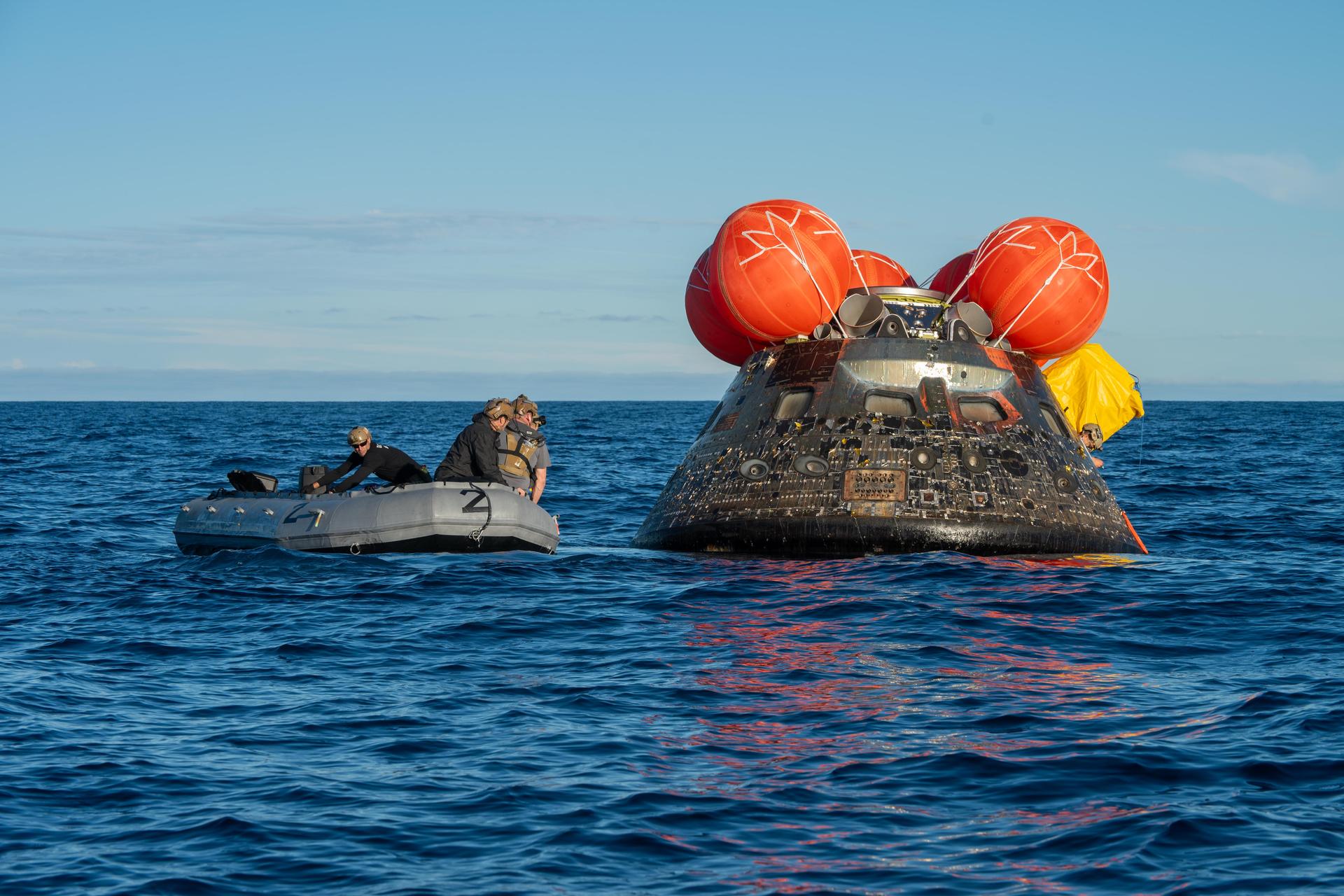NASA’s Landing and Recovery team and U.S. Navy personnel aboard an inflatable raft approaching the Orion spacecraft shortly after splashdown, helping the crew out of the capsule.