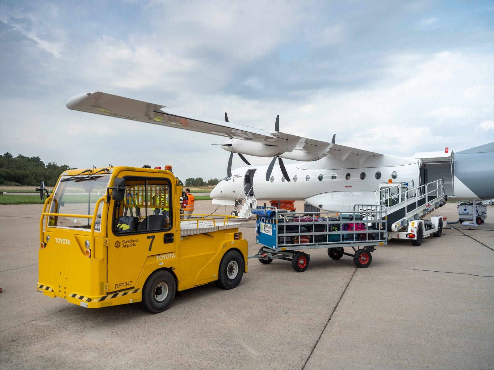 The Heart Aerospace X1 prototype on the apron during a ground-handling test, with a tow tug, baggage cart and passenger stairs alongside it.