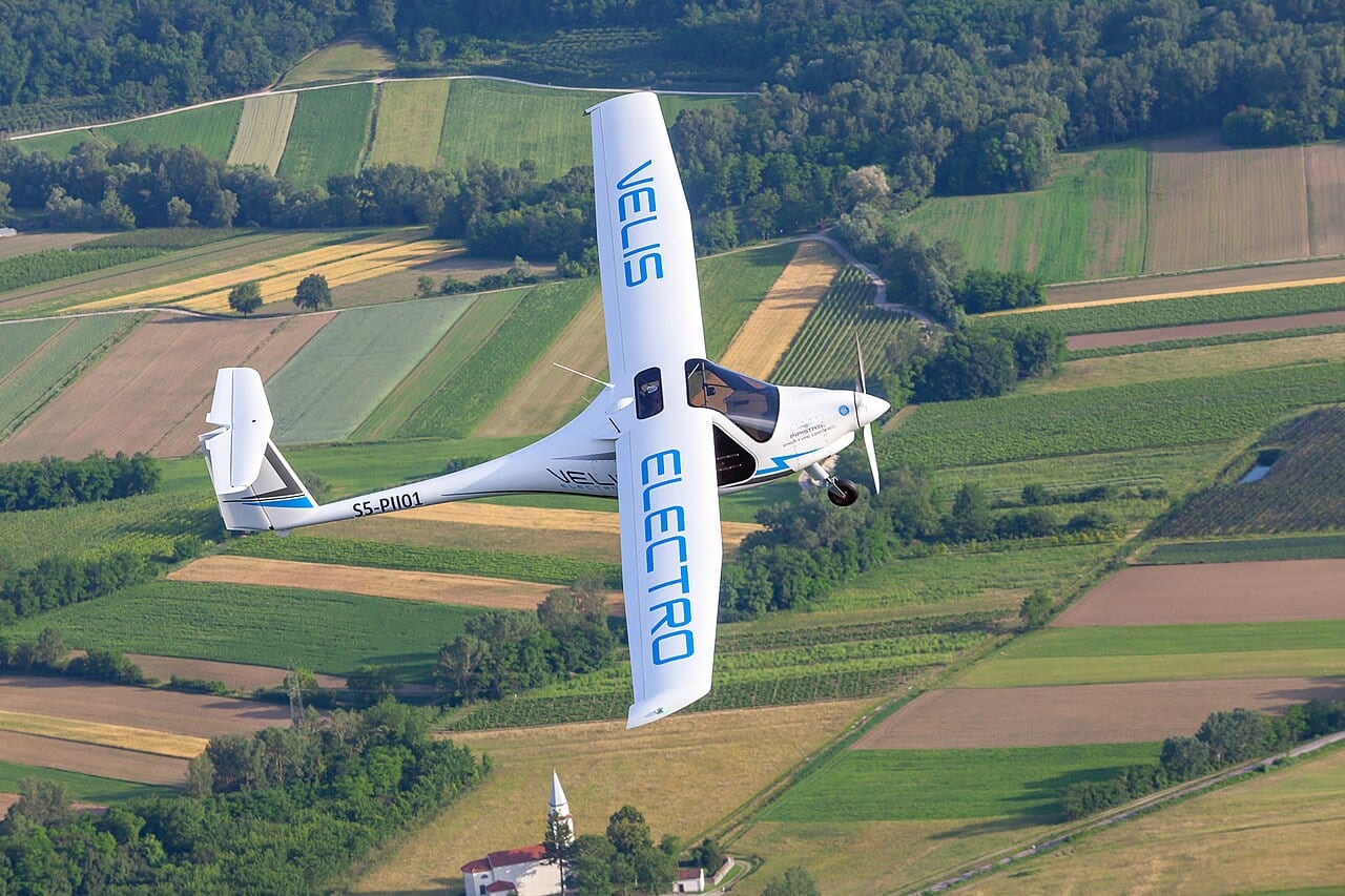 A Pipistrel Velis Electro two-seat electric aircraft on the ground, its small size visible next to the surrounding airfield equipment.