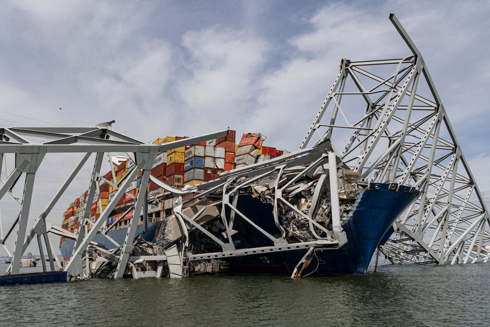 Collapsed steel trusses of the Francis Scott Key Bridge resting on the bow of the container ship Dali, its containers visible behind the wreckage.
