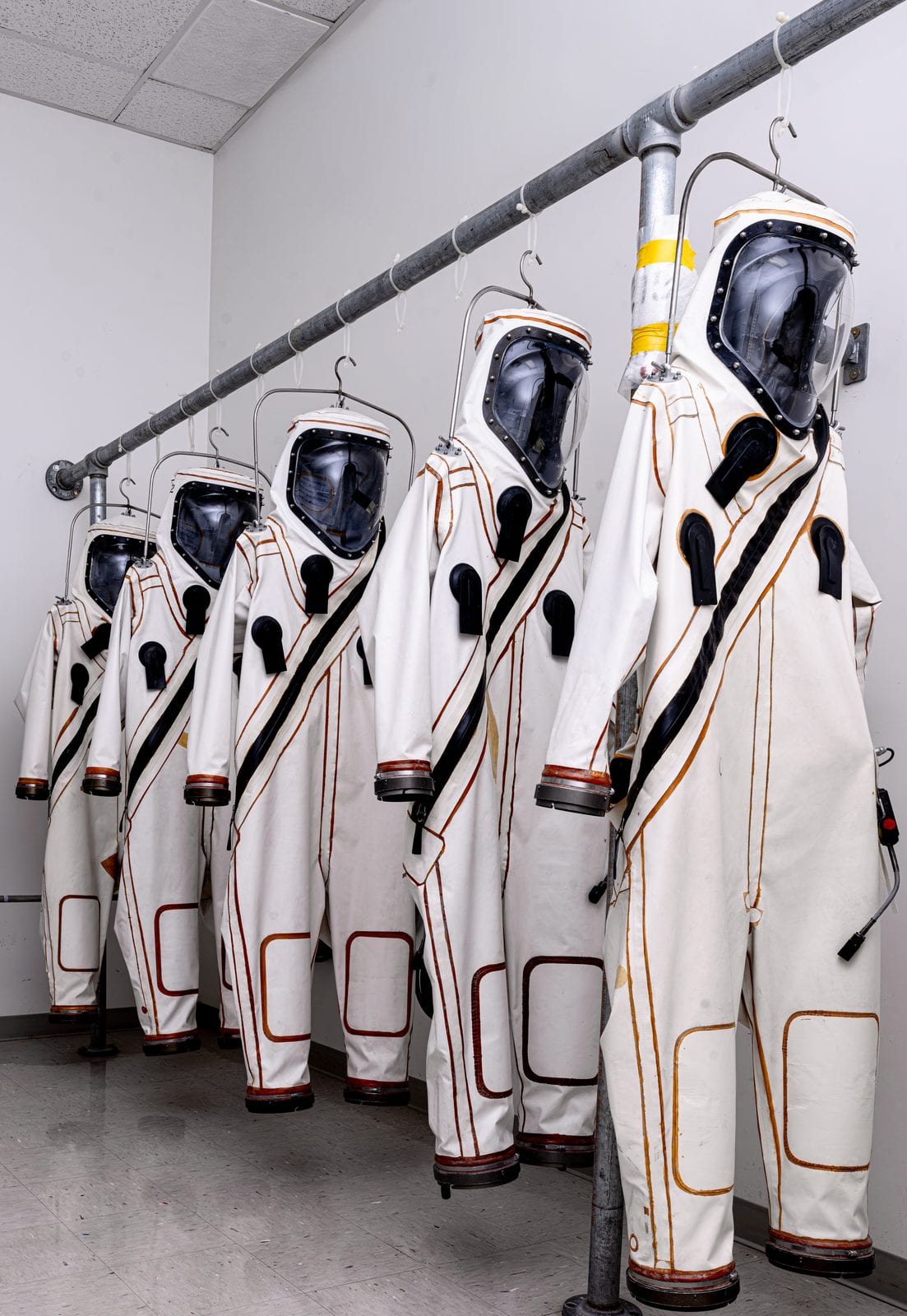 A row of white protective SCAPE suits hanging in a Kennedy Space Center facility, worn by technicians loading hydrazine propellant into the Roman Space Telescope.