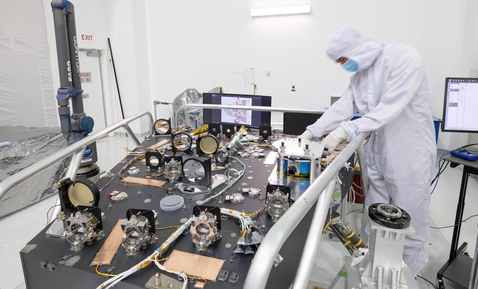 Engineer Jordan Rupp with the optical bench for the Coronagraph Instrument on the Nancy Grace Roman Space Telescope at NASA’s Jet Propulsion Laboratory.