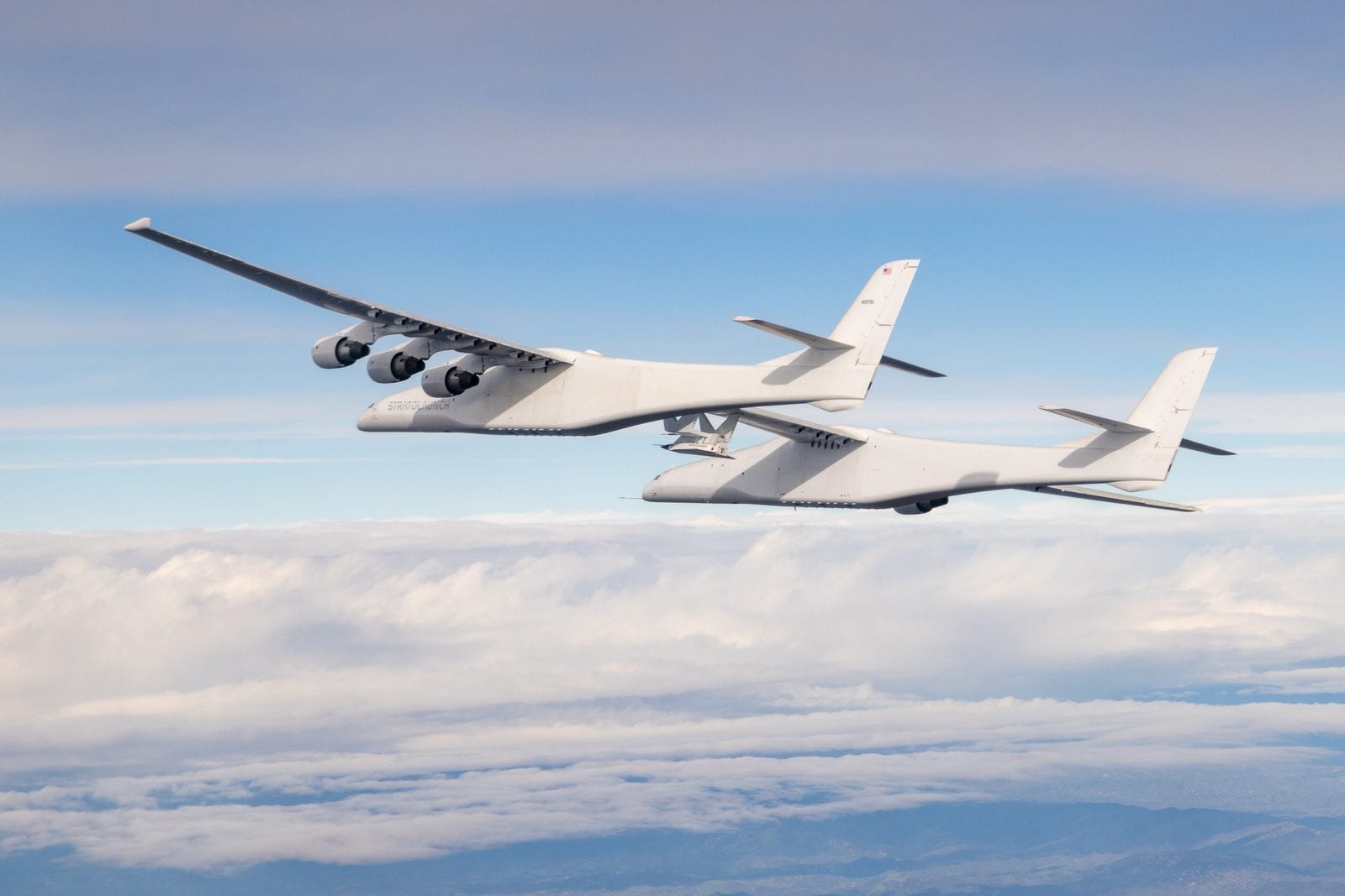 Stratolaunch’s twin-fuselage Roc carrier aircraft in flight above clouds, with a Talon-A vehicle mounted under its centre wing.