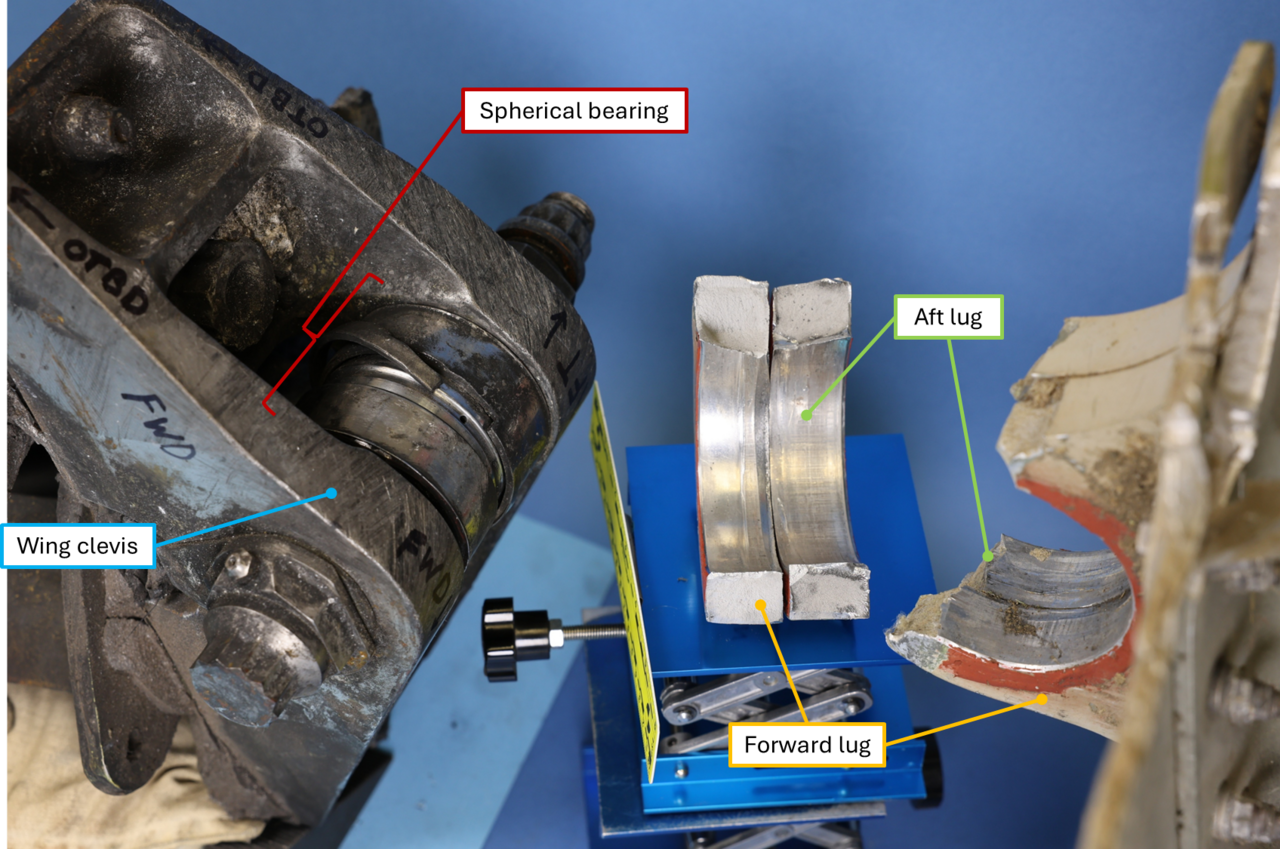NTSB investigation photo labeled with the wing clevis, spherical bearing, and the fractured forward and aft lugs recovered from the left pylon aft mount.